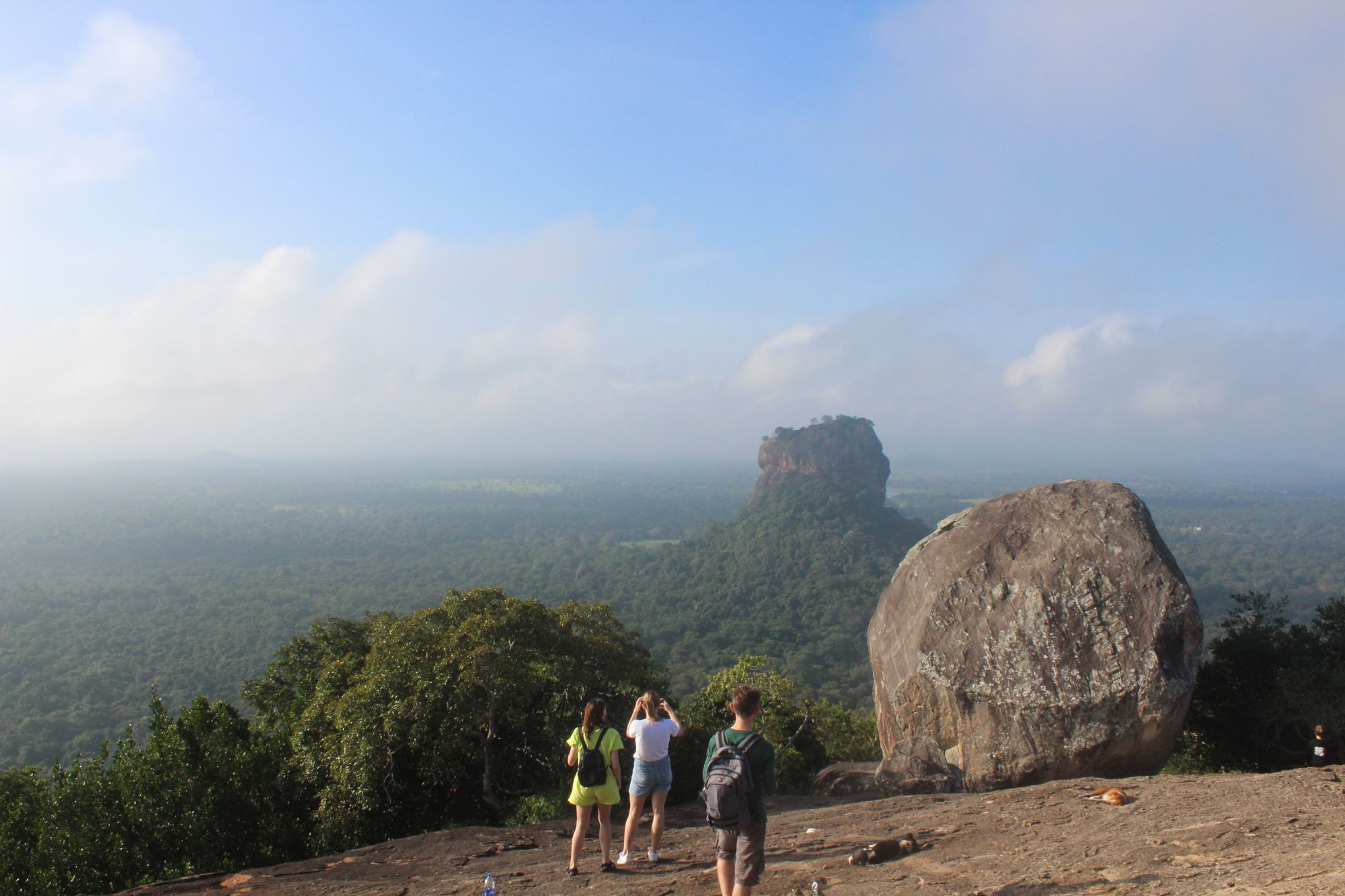 Tourists admiring the surroundings from Pidurangala Rock with Sigiriya Rock in the background.